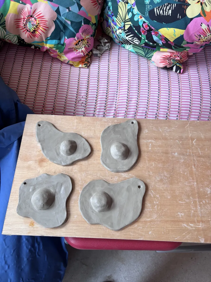 Four unfired clay fried-egg wall hangings drying on a board