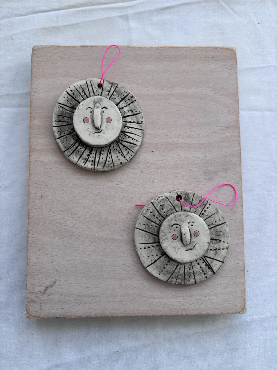 Two sun-face hangings with rosy cheeks on a pink board