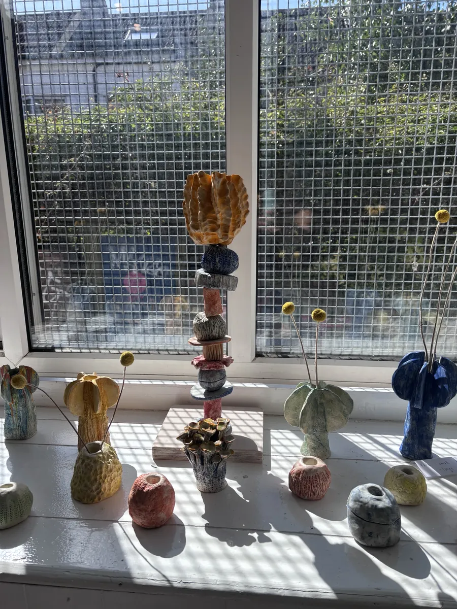 A tall stacked totem among textured vases on a sunny windowsill