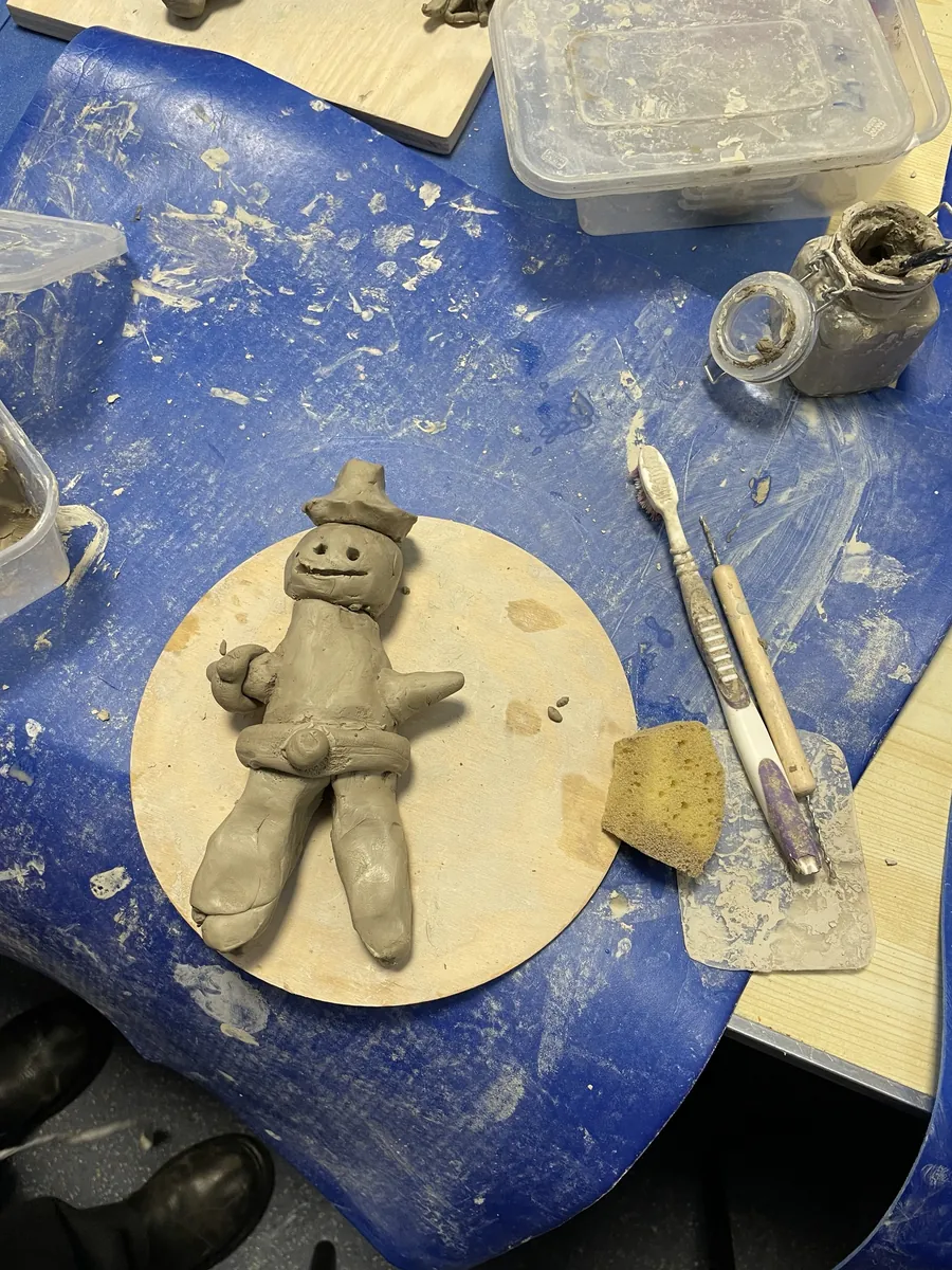 An unfired clay cowboy in a hat, drying on a board