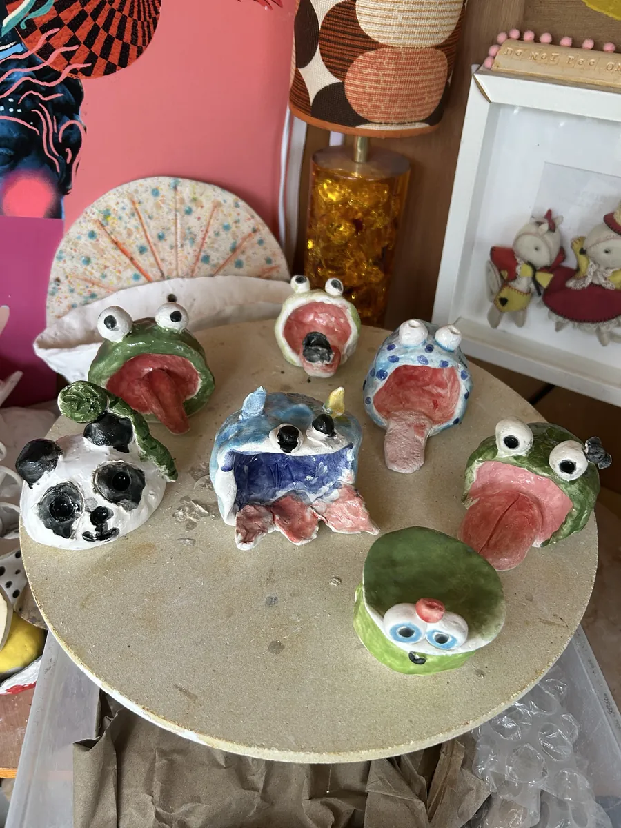 Big-mouthed glazed frogs, a panda and a monster on a kiln shelf