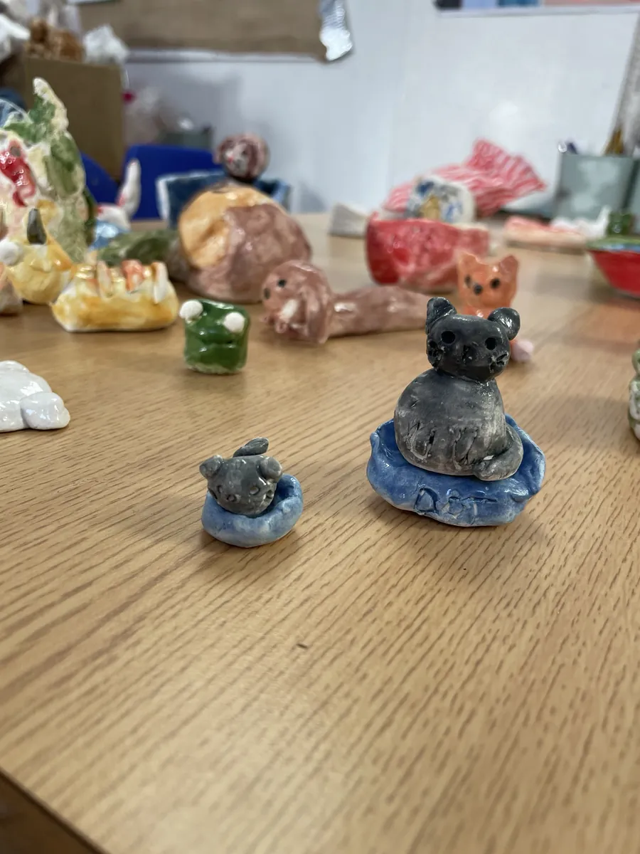 Two grey clay cats sitting in little blue beds