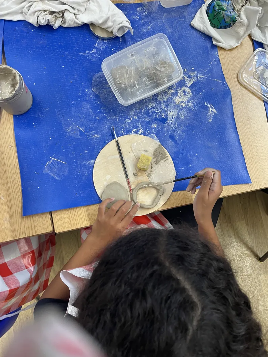 A child joining clay coils with slip and a fine brush