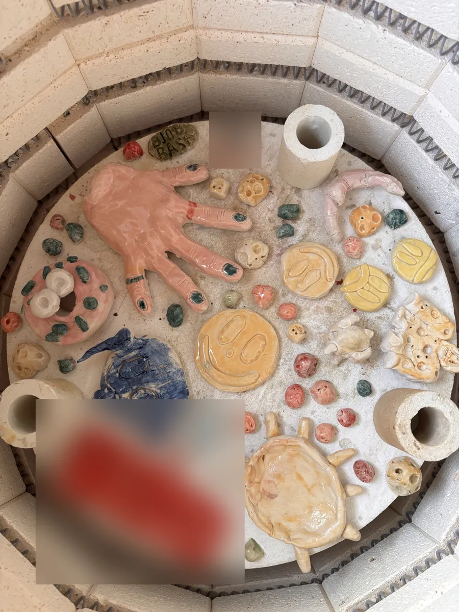 A kiln shelf with a glazed hand, smiley faces and lots of little beads