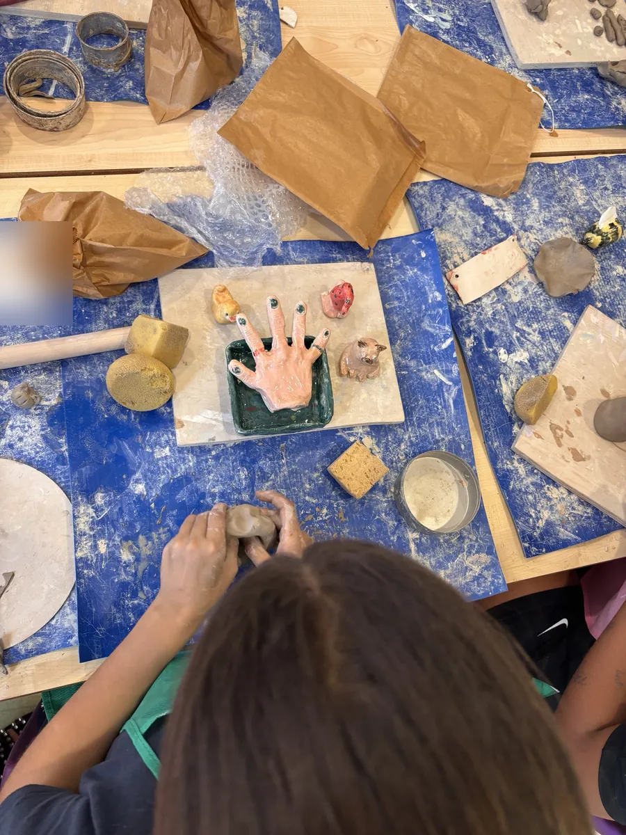 A child working clay beside a finished glazed hand in a green dish