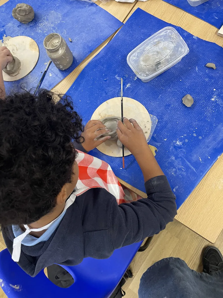 A child smoothing a coil pot with a brush, seen from above