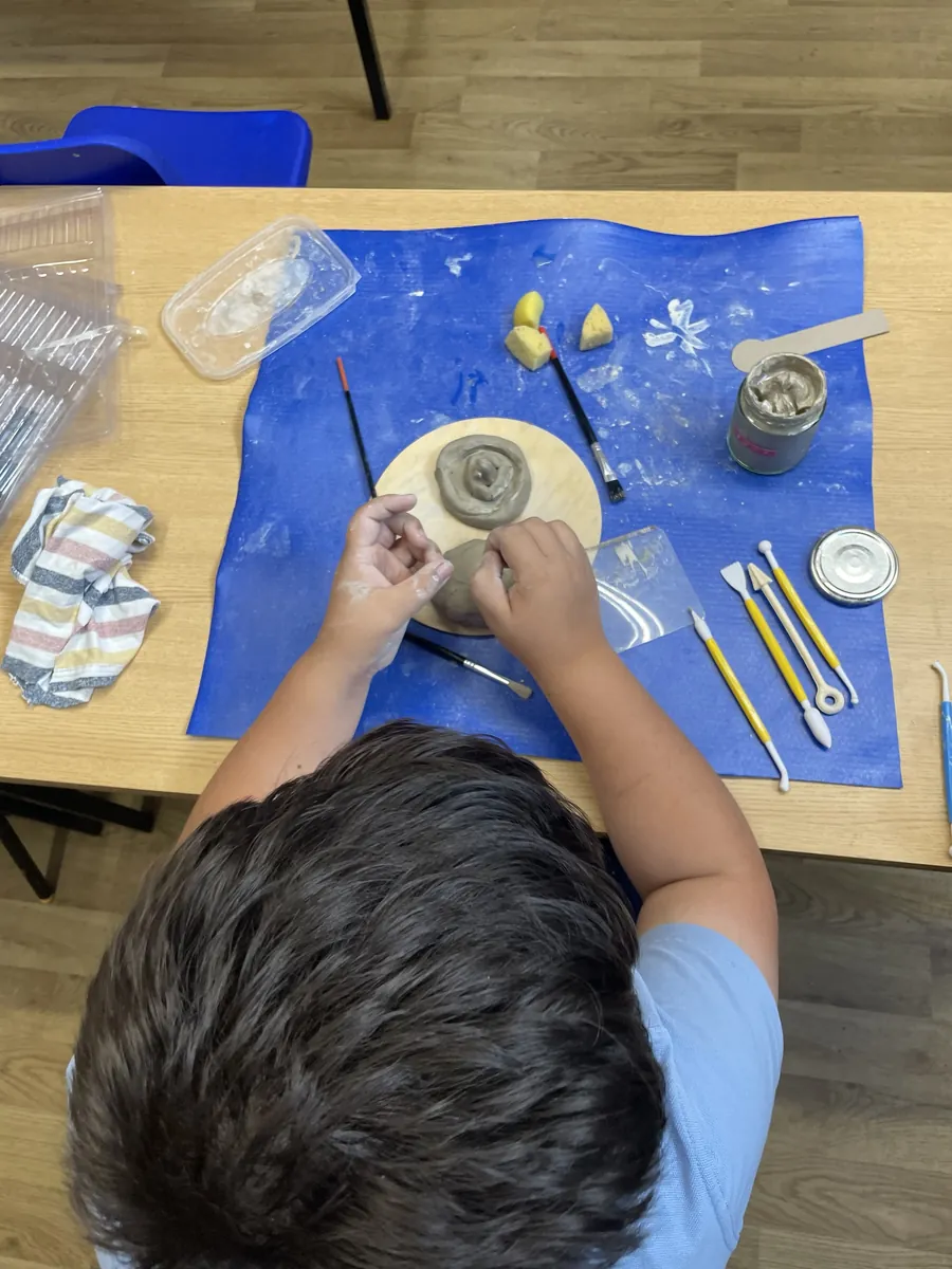 A child building a clay spiral, with tools laid out on the mat
