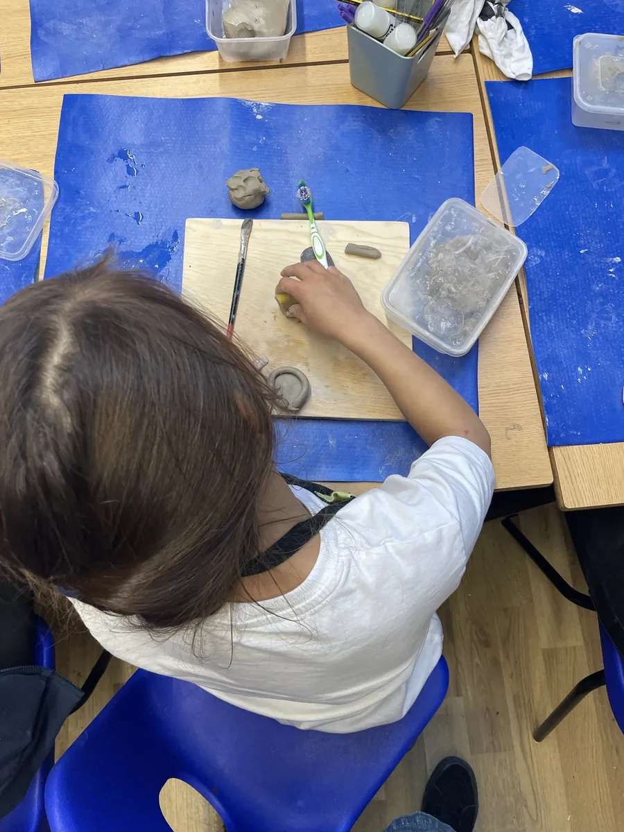 A child smoothing a small pinch pot with a sponge