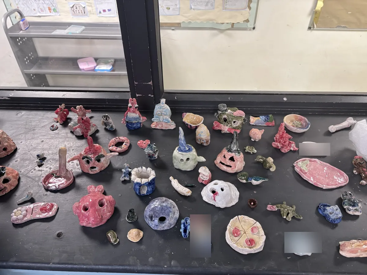 A tableful of children's glazed pieces: heads, pots, a pizza and name plaques