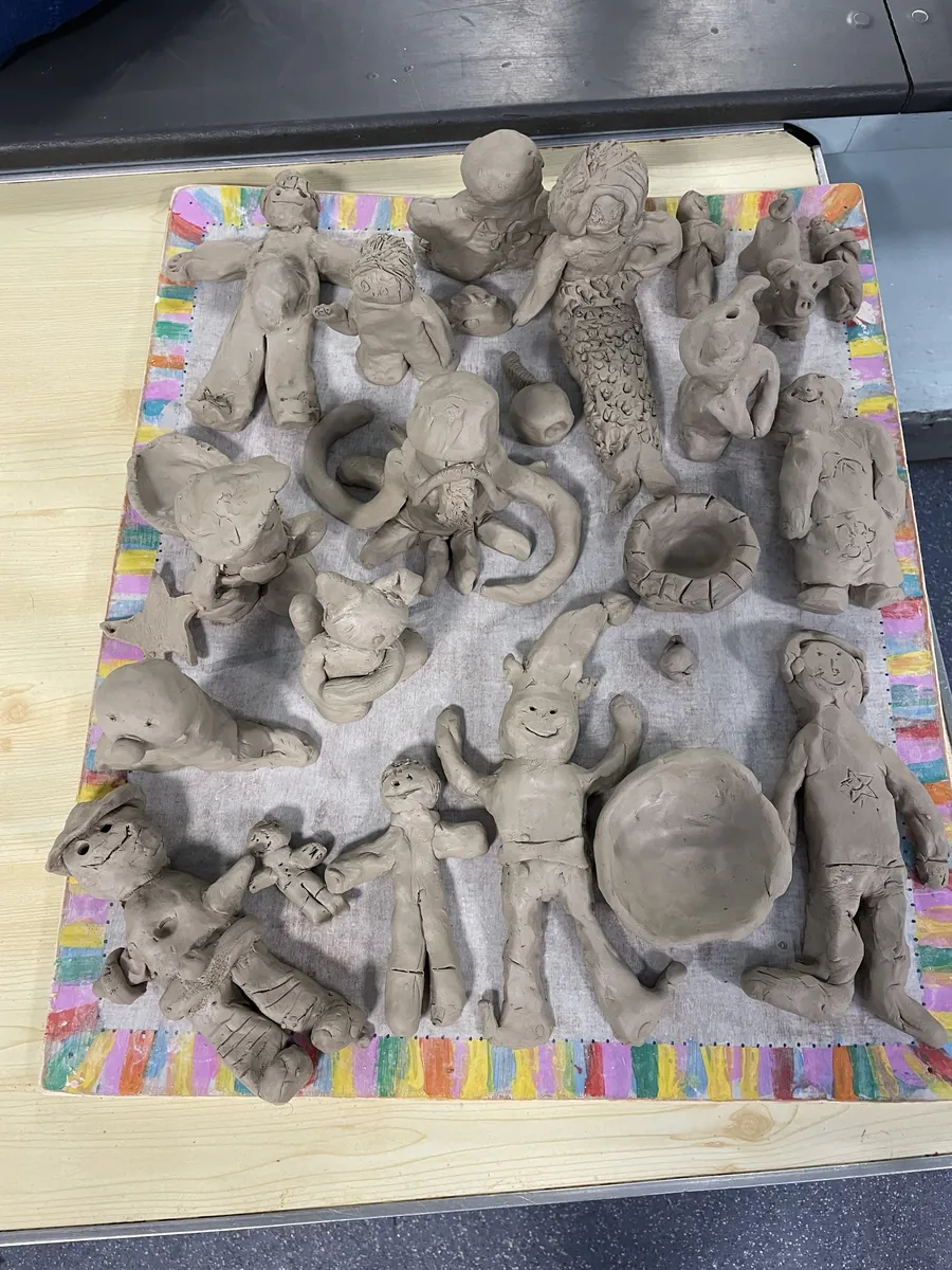 A rainbow-edged board full of unfired clay people and creatures