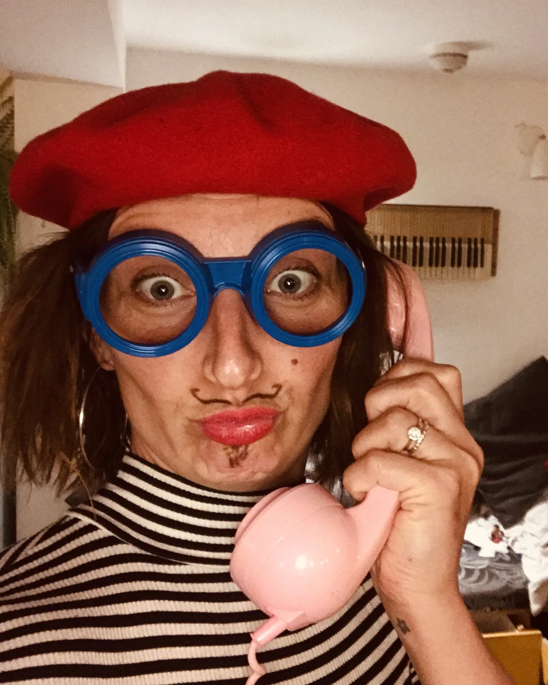 Gemma in a red beret, big blue glasses and a drawn-on moustache, pouting into a pink telephone