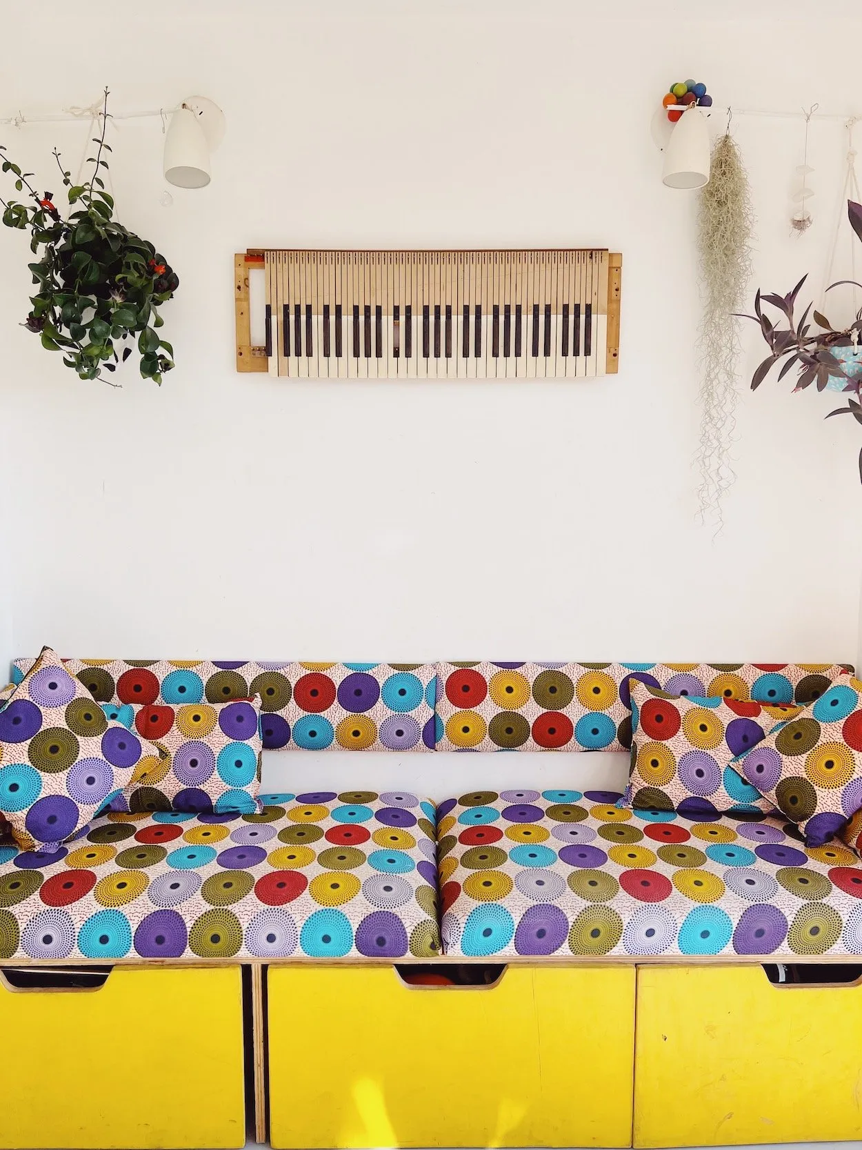 A bright room with a keyboard hung on the wall above a yellow bench seat in multicoloured circle-print fabric