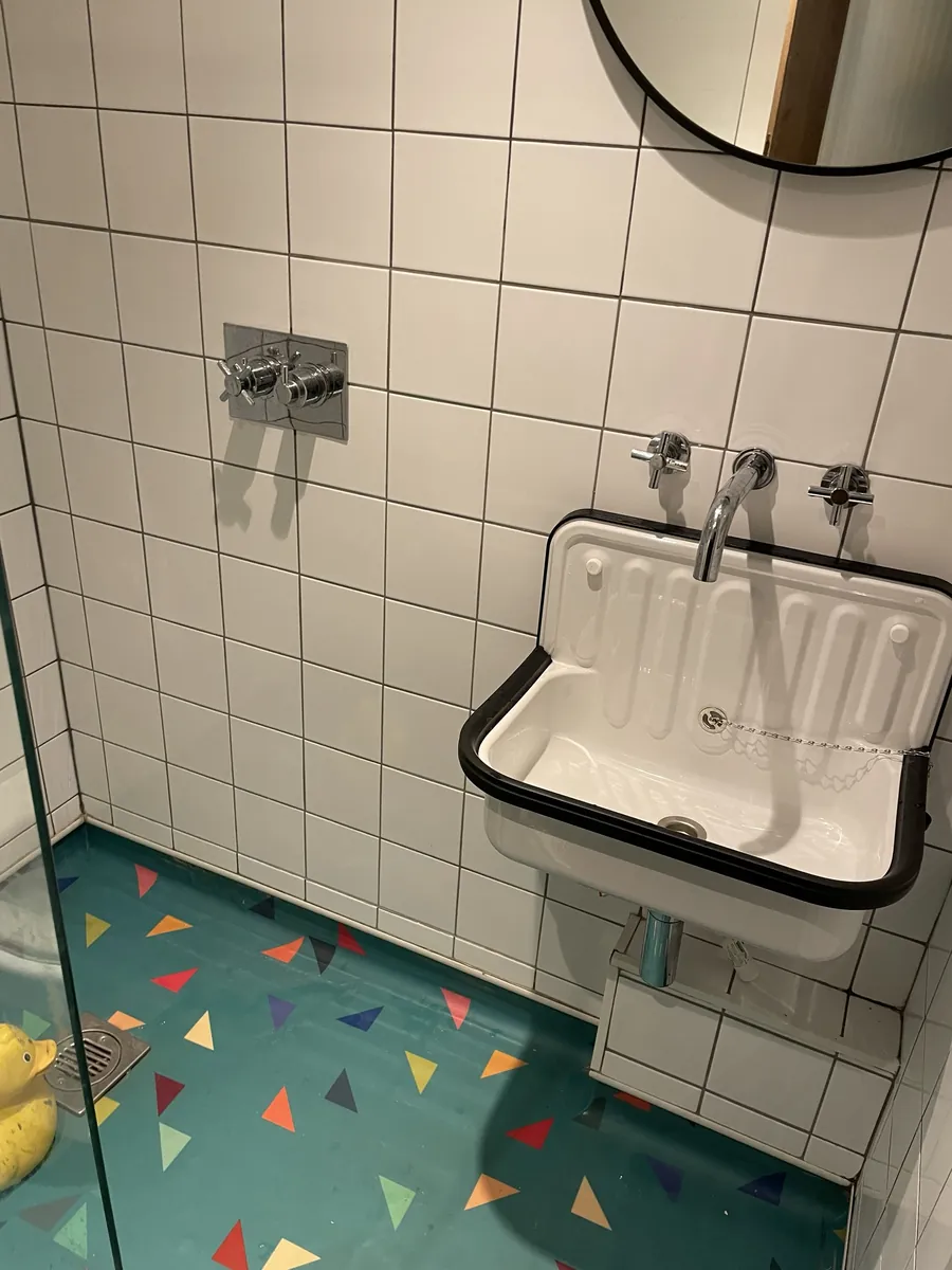 A vintage enamel sink against white tiles and a confetti-print floor