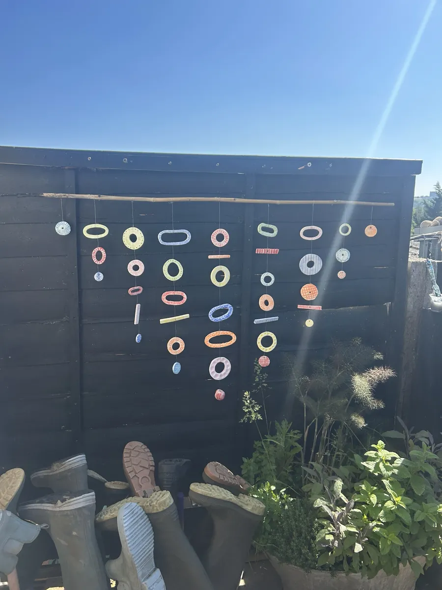 Painted ceramic rings and discs hung from a bamboo cane against a black fence