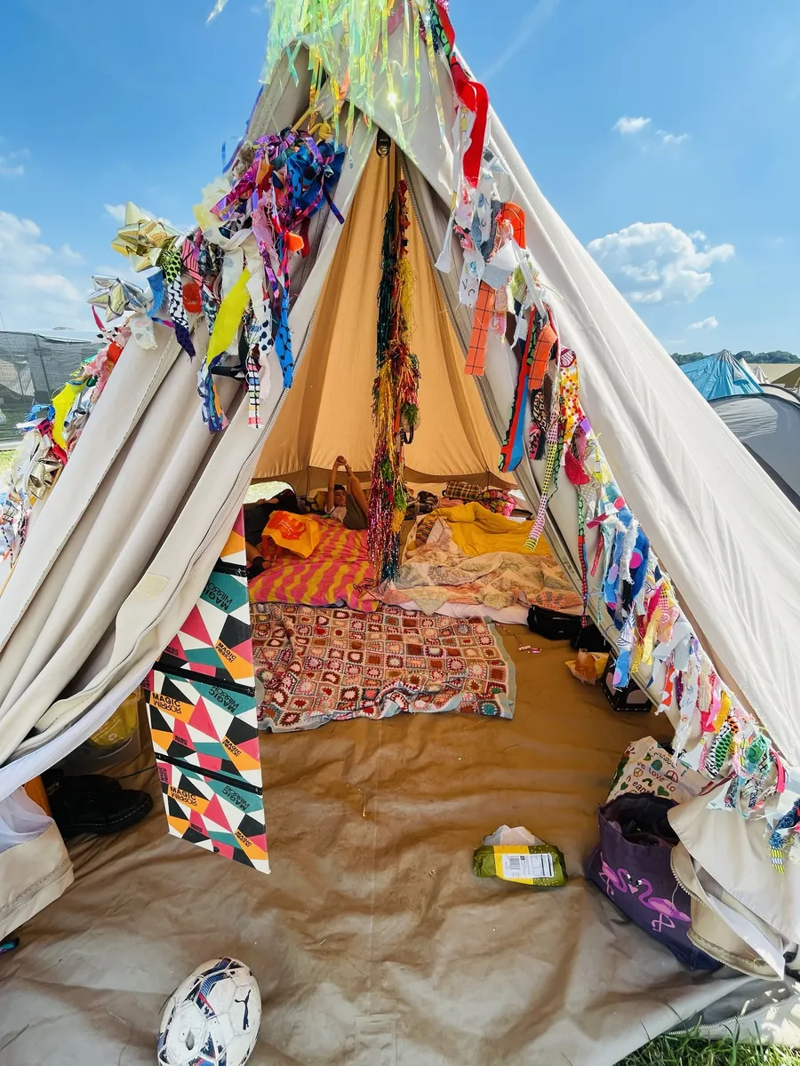 A bell tent decorated with fabric streamers, rugs and blankets