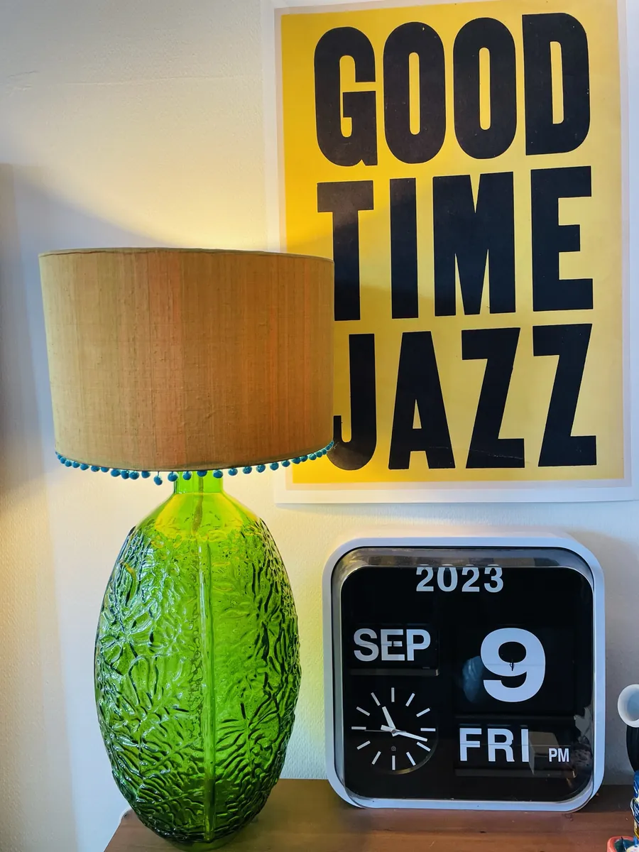 A green glass lamp with a pom-pom shade beside a Good Time Jazz poster