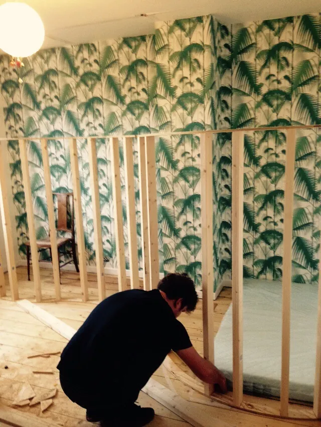 Building a curved timber den against green palm-leaf wallpaper