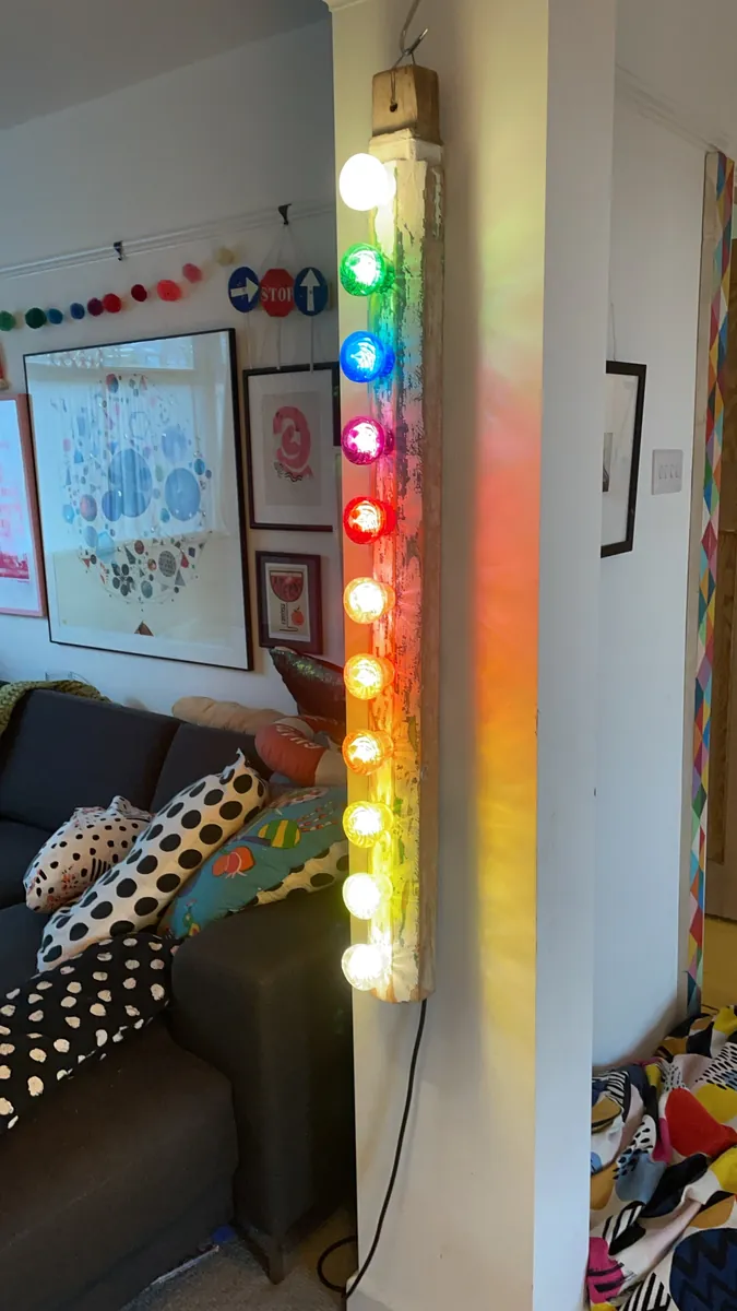 A reclaimed wooden post lit with a column of rainbow bulbs