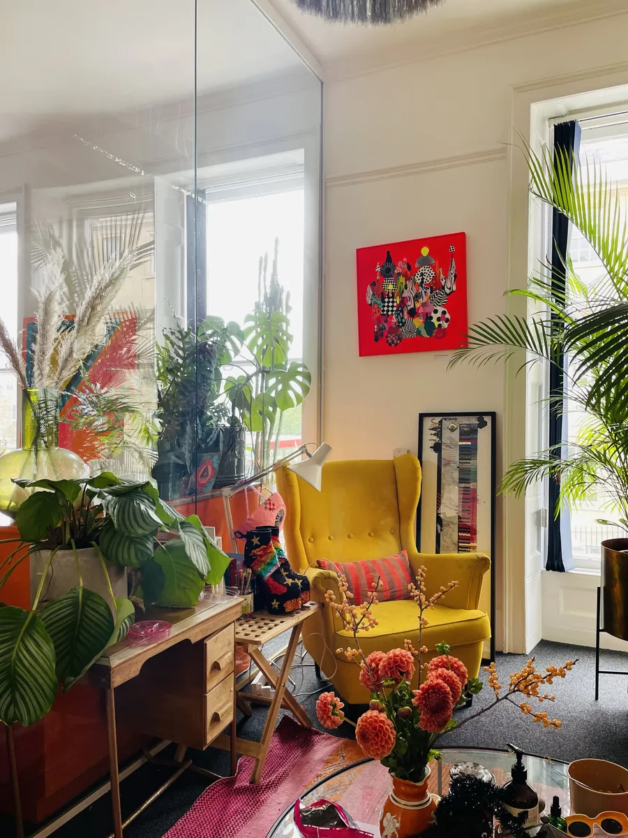 A yellow wingback chair, red artwork and big plants in a bright office