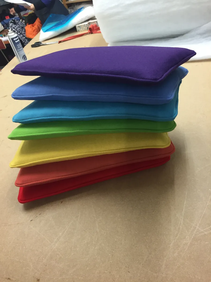 A stack of piped wool cushions in rainbow colours