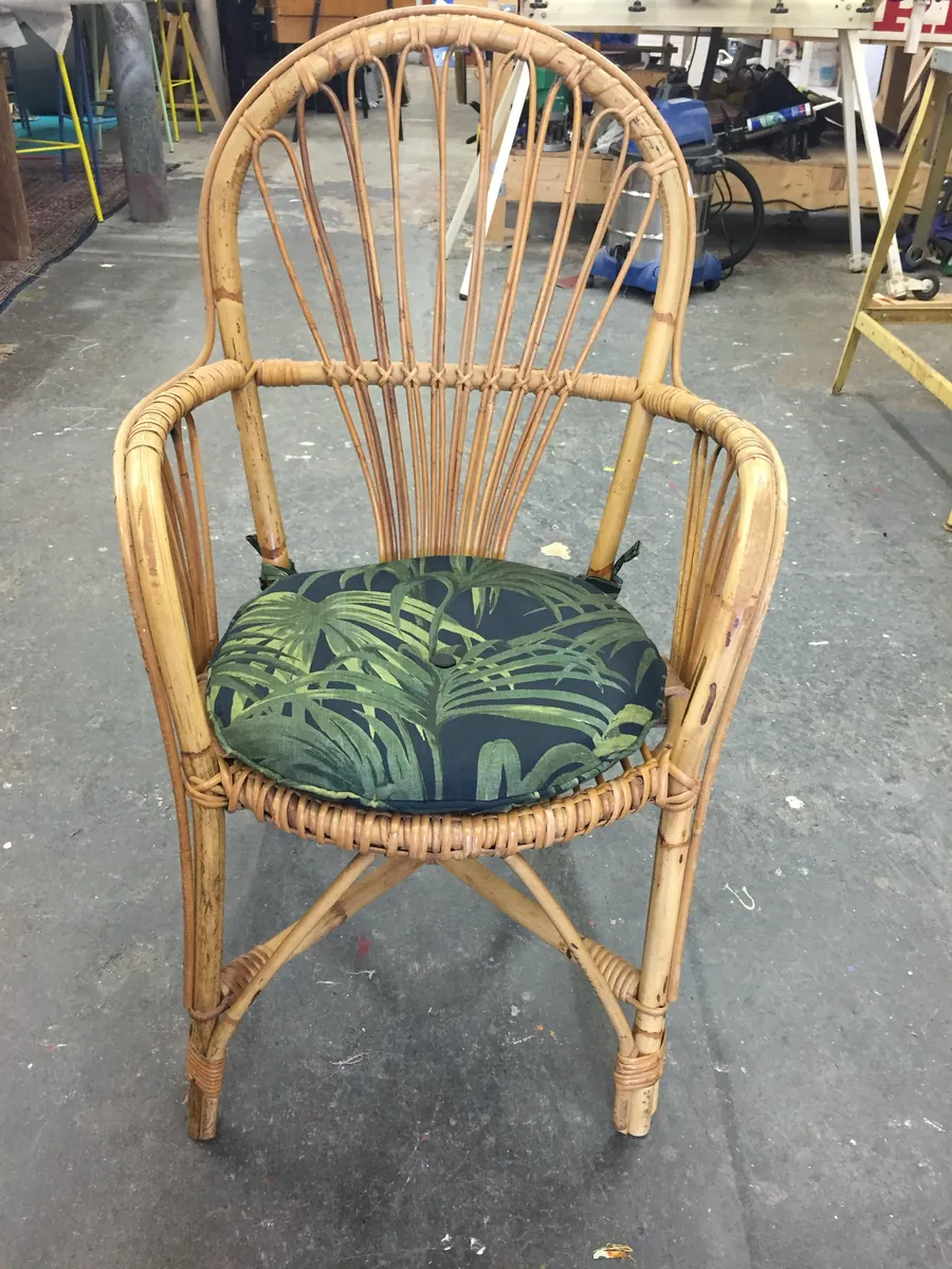 A rattan chair with a buttoned palm-print seat pad
